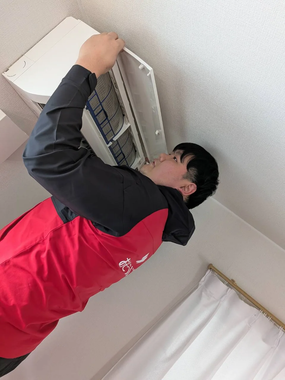 スタッフが壁掛けエアコンのカバーを開いて作業する様子